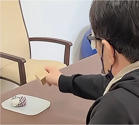 机の上の積み木に手を伸ばす利用者の後ろ姿。