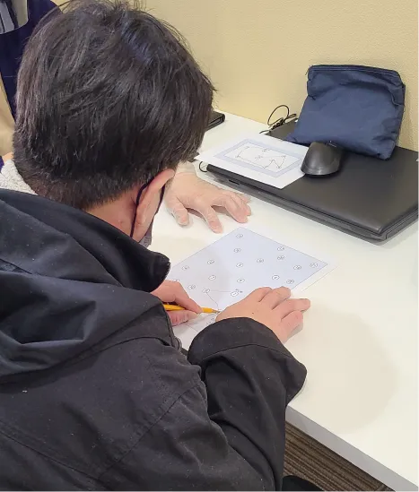 高次機能検査の風景。回答用紙に鉛筆で書き込む利用者。